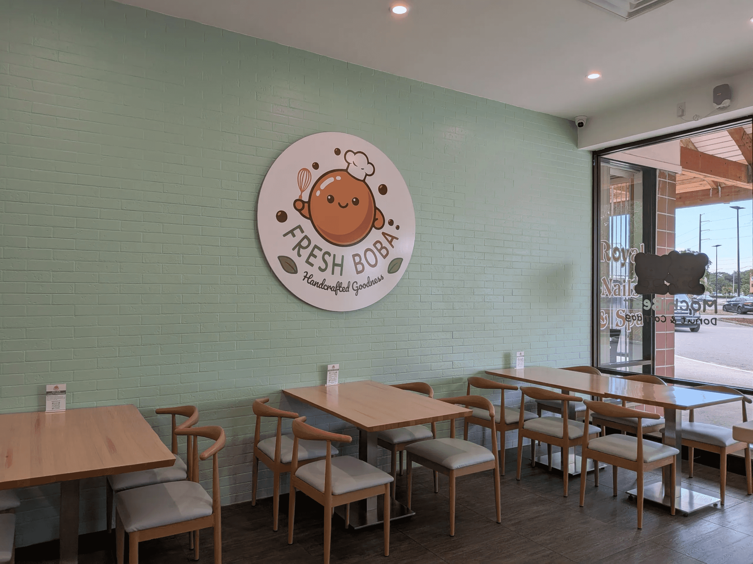 FRRSH BOBA interior with tables and chairs in front of a light green wall with a large, round FRESH BOBA logo.