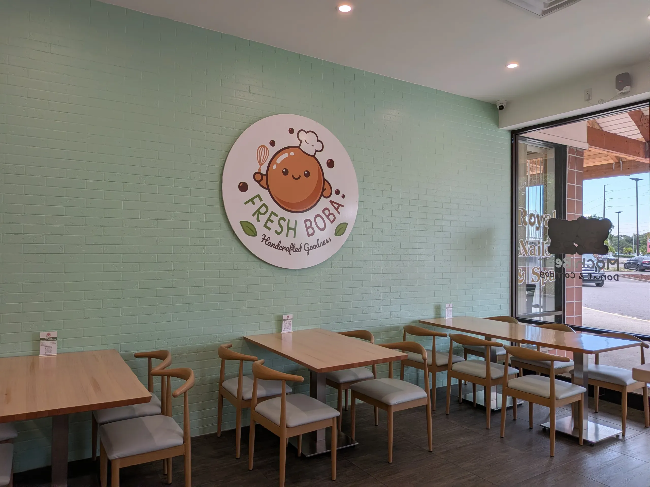 FRRSH BOBA interior with tables and chairs in front of a light green wall with a large, round FRESH BOBA logo.
