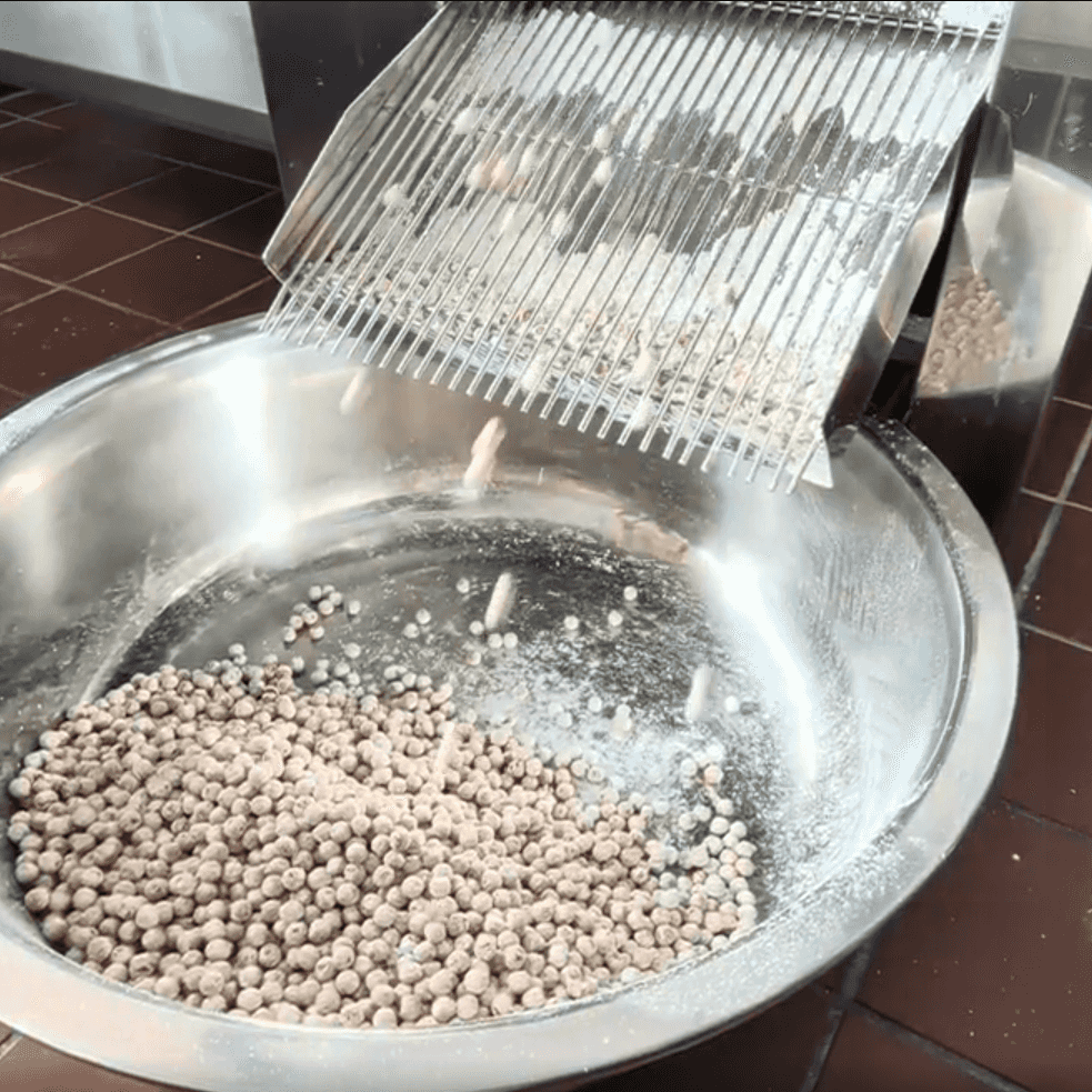 A close-up of fresh-cut boba pearls tumbling down a grilled ramp belonging to an imported boba cutting machine