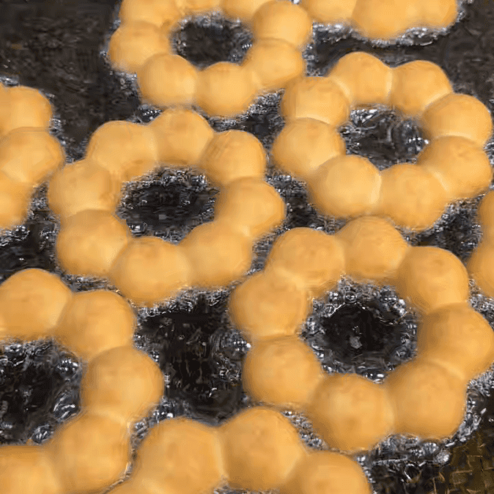 Golden mochi donuts frying in oil, showcasing their signature "pon-de-ring" shape and perfectly bubbly texture.